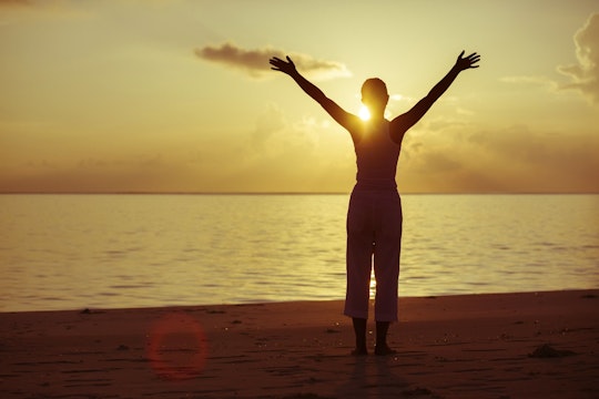 Slim woman holding hands above hand in front of sunset over ocean