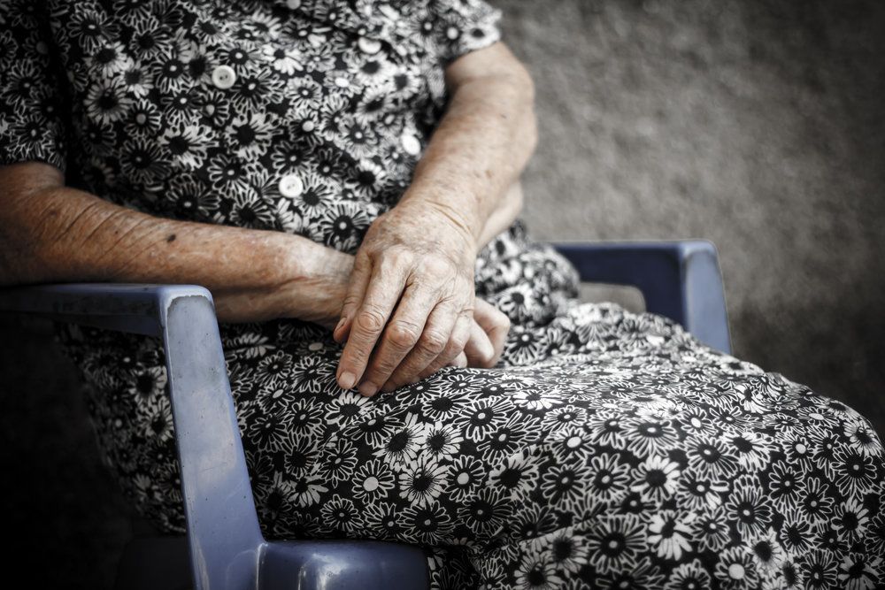 Elderly woman wearing flowered dress and sitting with arms crossed