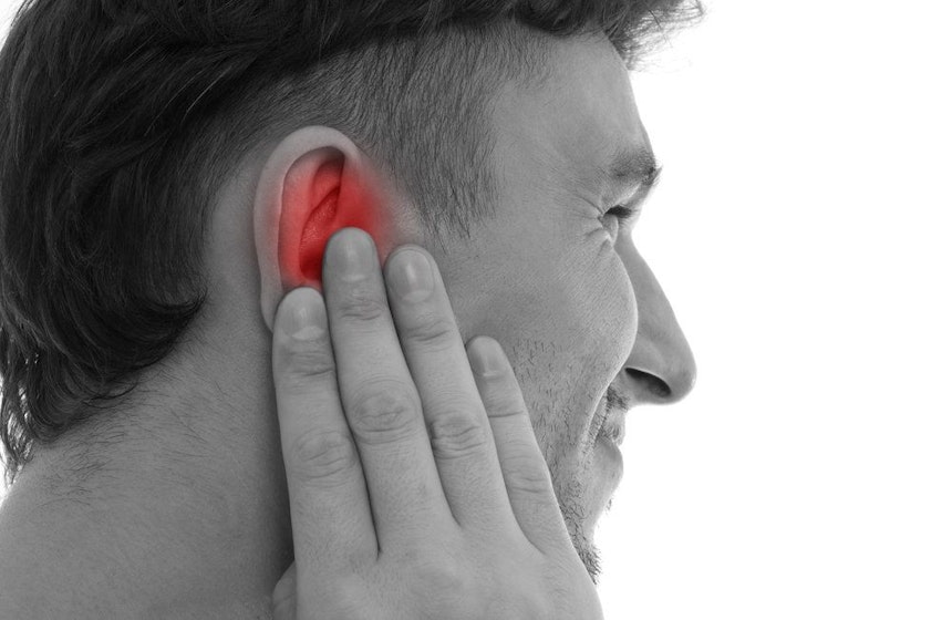 Man wincing and holding ear highlighted in red