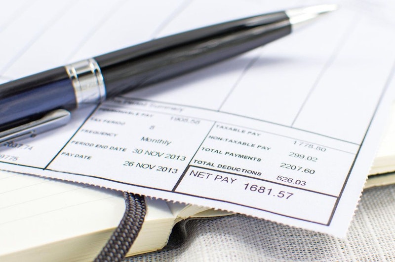 A pen sits on top of a paycheck stub