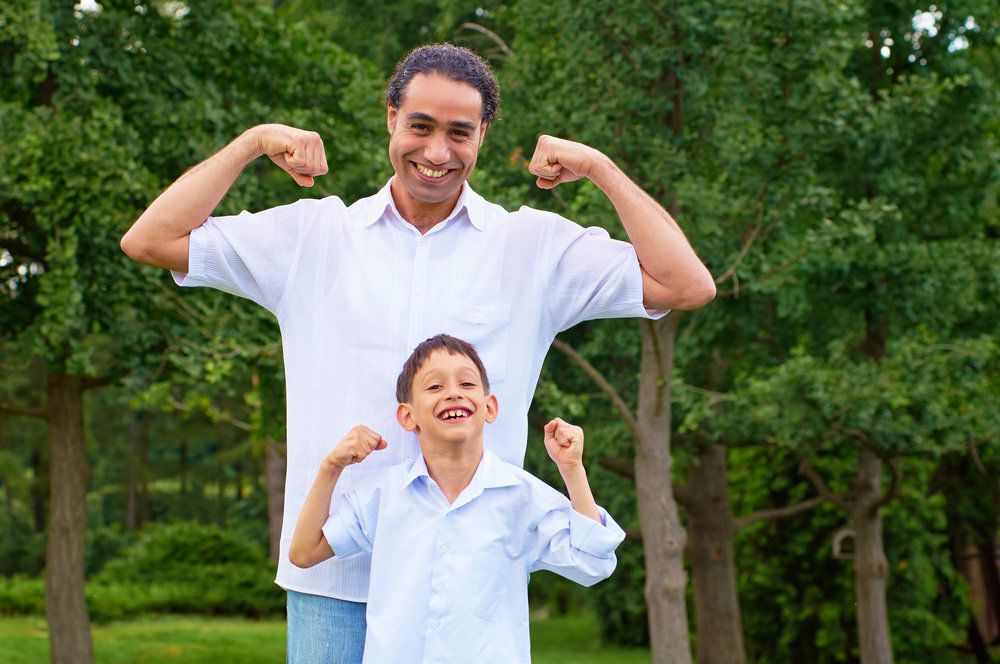 Happy father and son flexing muscles outdoors