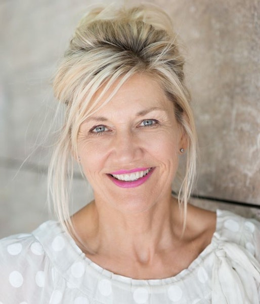 Middle aged woman smiling, standing in front of a cement wall
