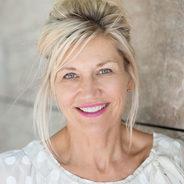 Middle aged woman smiling, standing in front of a cement wall