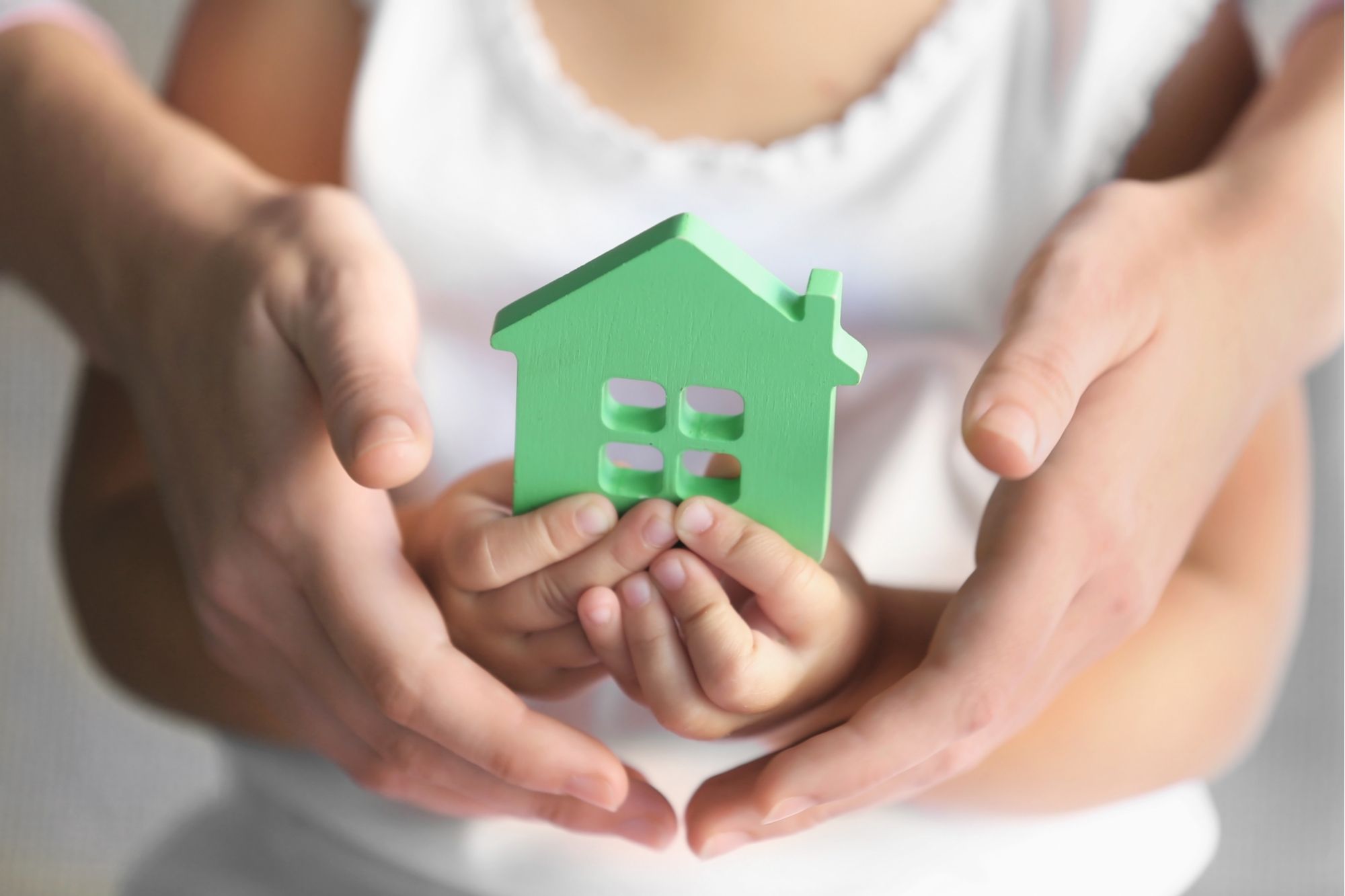 Child holding block in shape of house with adult cradling their hands