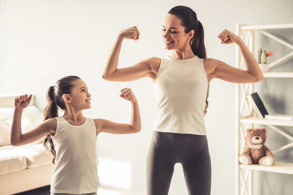 fit woman flexing her muscles with a little girl