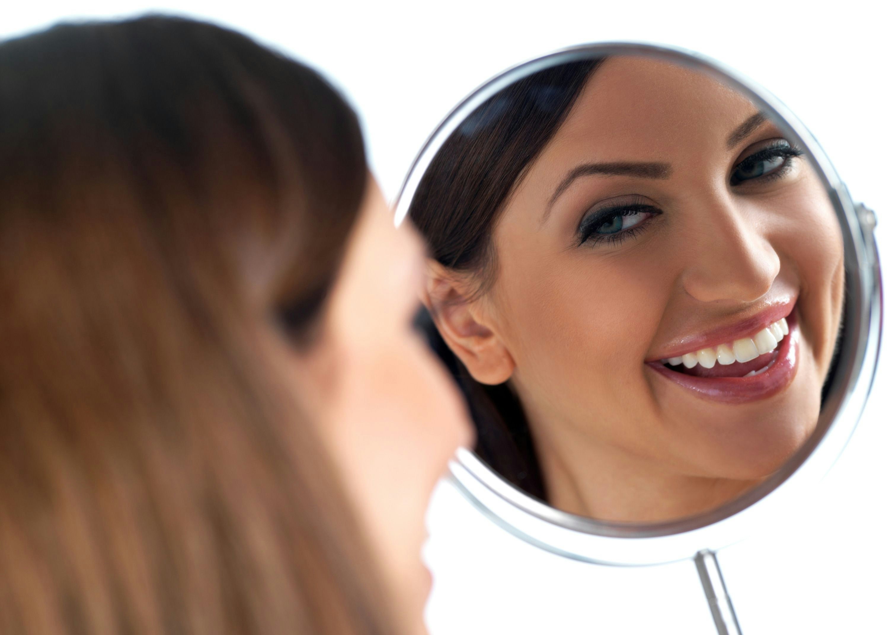 Woman smiling into handheld mirror