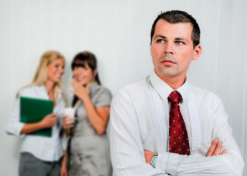 A man crosses his arms defensively while two women whisper in the background.