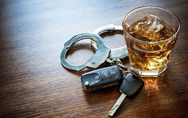 glass of dark liquor, car keys, and handcuffs on wooden table