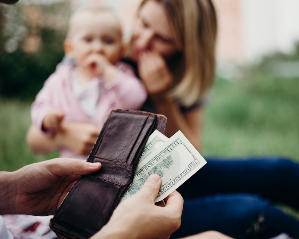 Person pulling out money from wallet, with baby and mom in the background