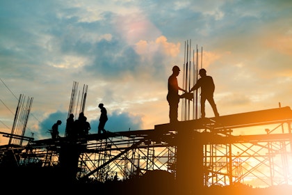 Workers standing on scaffolding against sunset