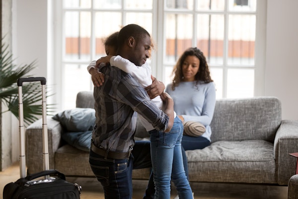 Daughter hugging custodial parent goodbye with other parent in the background