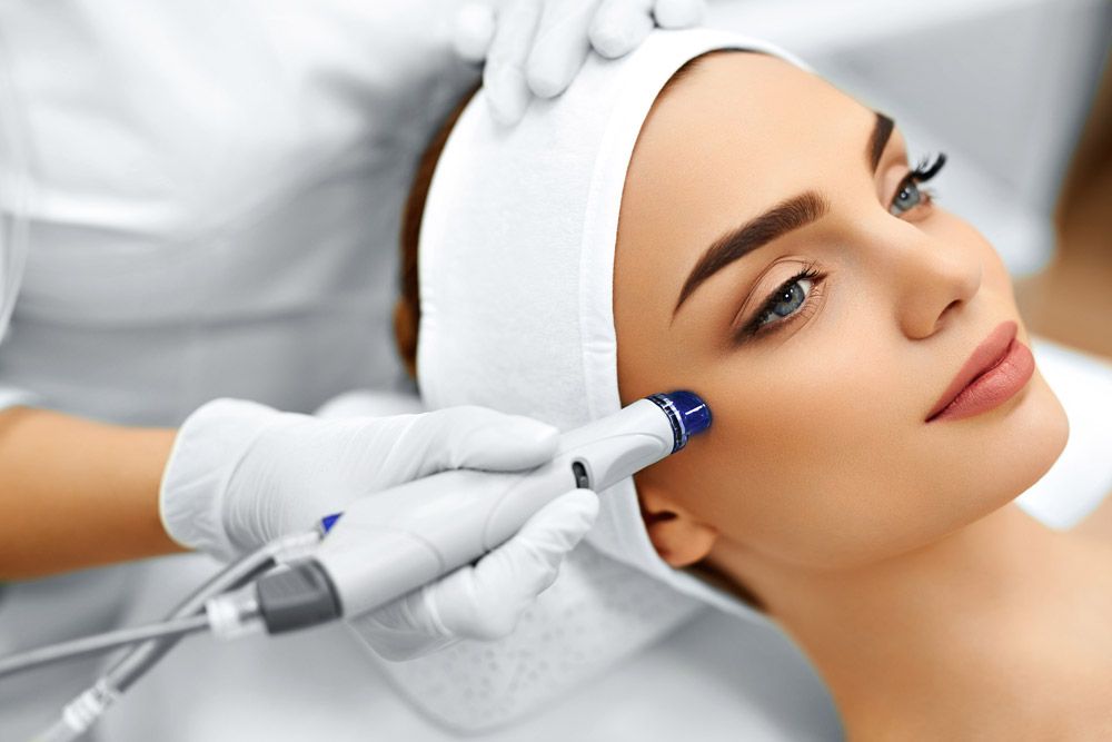 Woman with clear skin receiving a HydraFacial on her right cheek