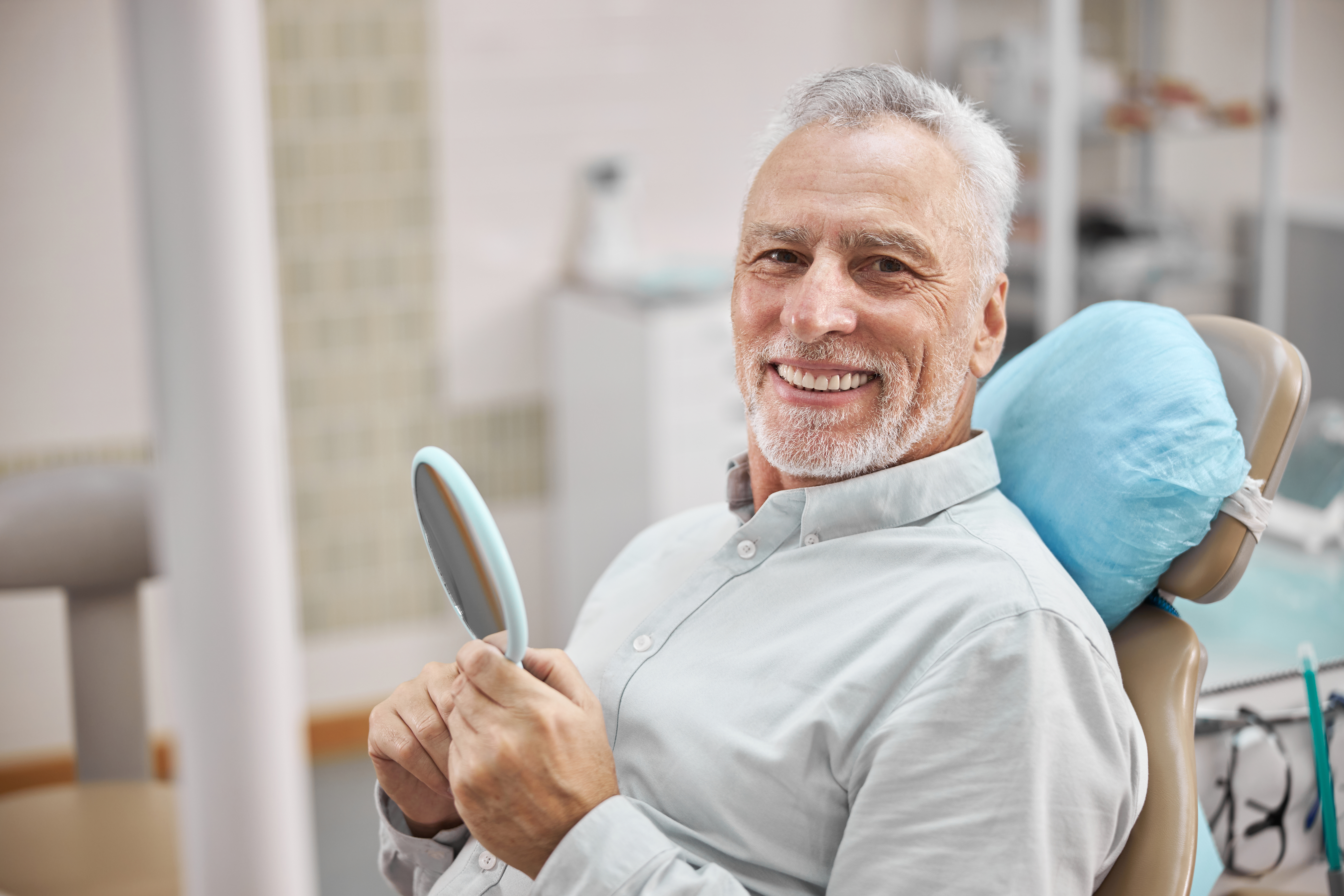 Smiling older man in dental chair holding hand mirror