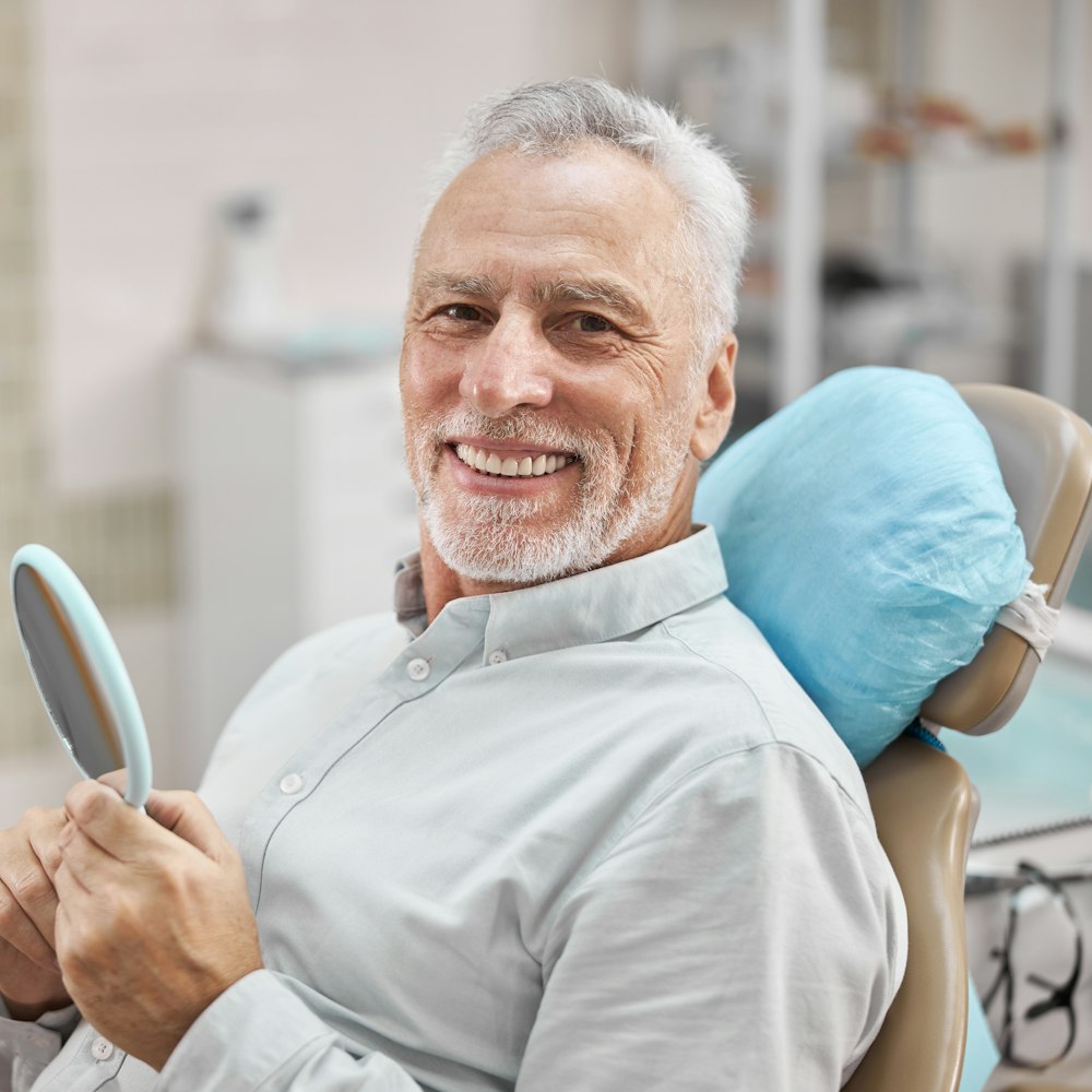 Smiling older man in dental chair holding hand mirror