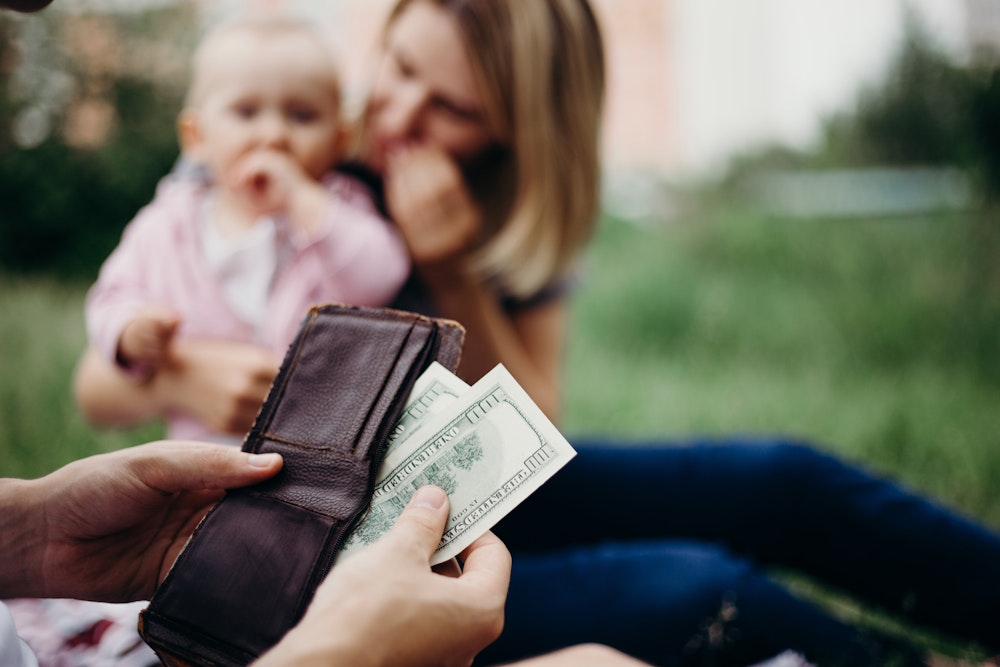 Person pulling out cash from their wallet with mom and baby in background