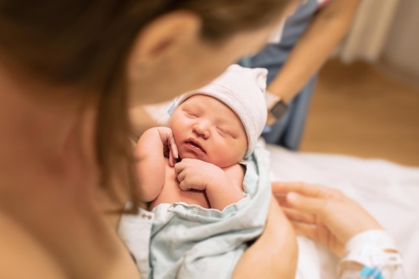 Baby with upper arms folded up being held by mother