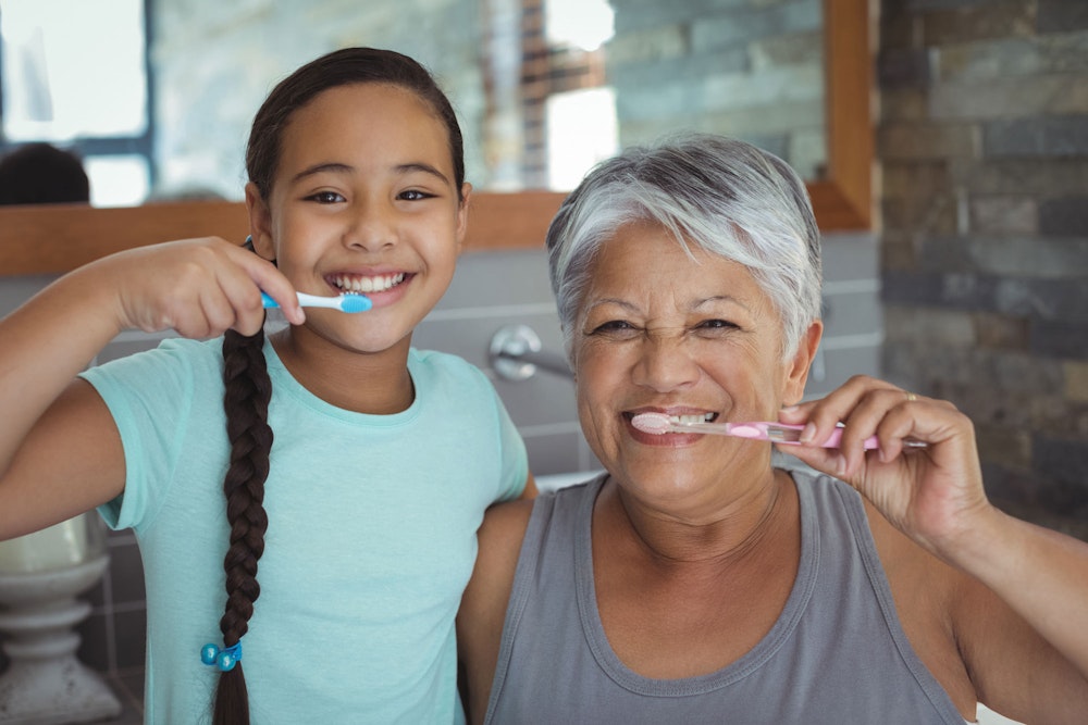 Mature woman and young child brushing teeth