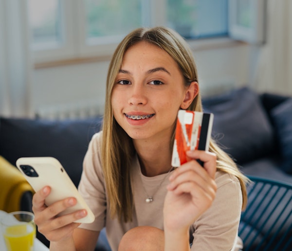 Smiling teenager holding smart phone and credit card