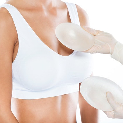 Doctor holding two round breast implants to woman in white bra