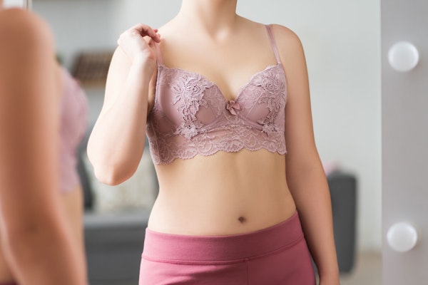 Woman wearing pink lace bra and yoga pants looking in the mirror