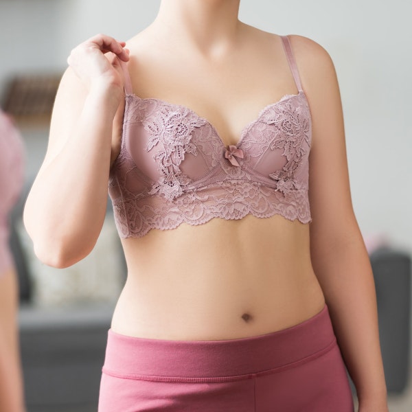 Woman wearing pink lace bra and yoga pants looking in the mirror