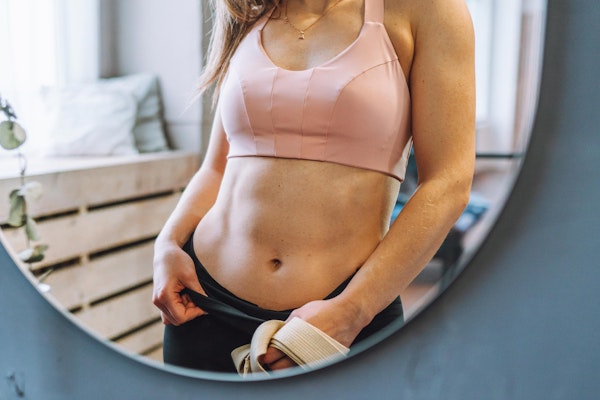 Woman wearing pink bra and black pants looking into a mirror
