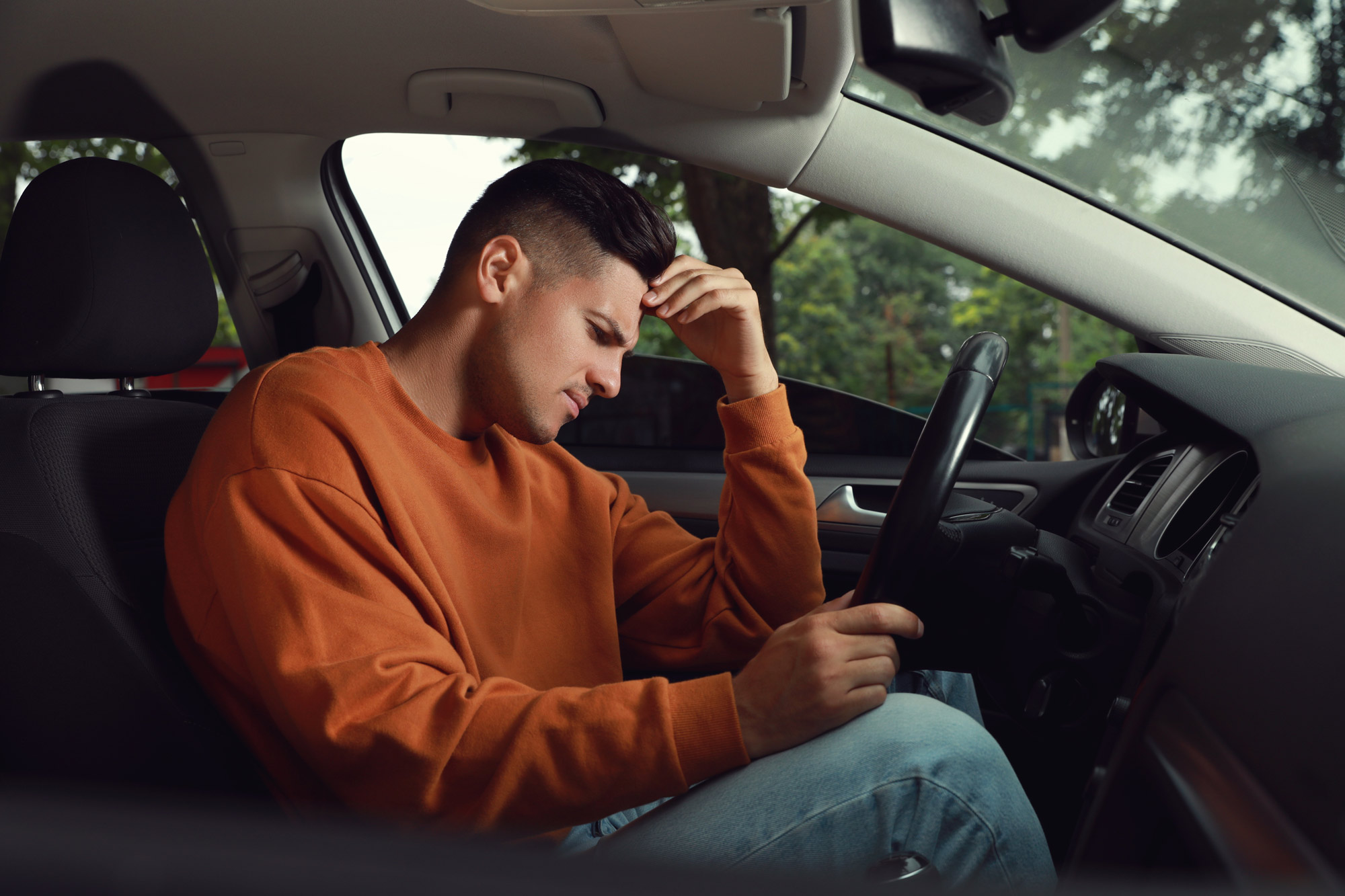 man sitting in a car with a furrowed brow and his hand on his forehead