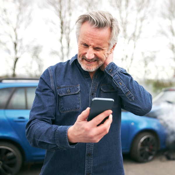 Man holding in neck looking at phone after car crash