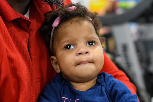 Baby wearing blue shirt with cerebral palsy sitting on someones lap