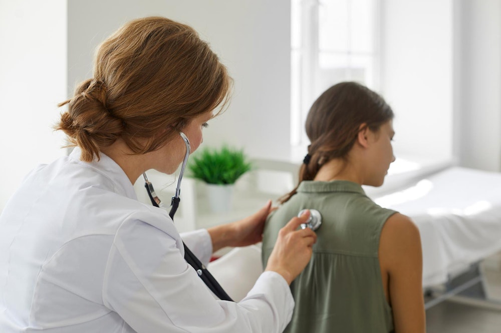 Doctor using stethoscope to listen to young girl's back
