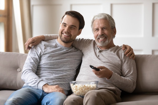 Mature man and adult son watching a movie with popcorn