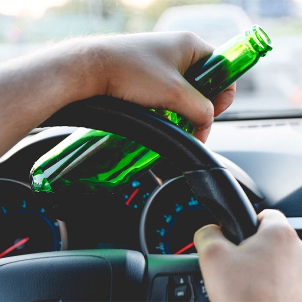 Driver with one hand on wheel and other holding beer bottle