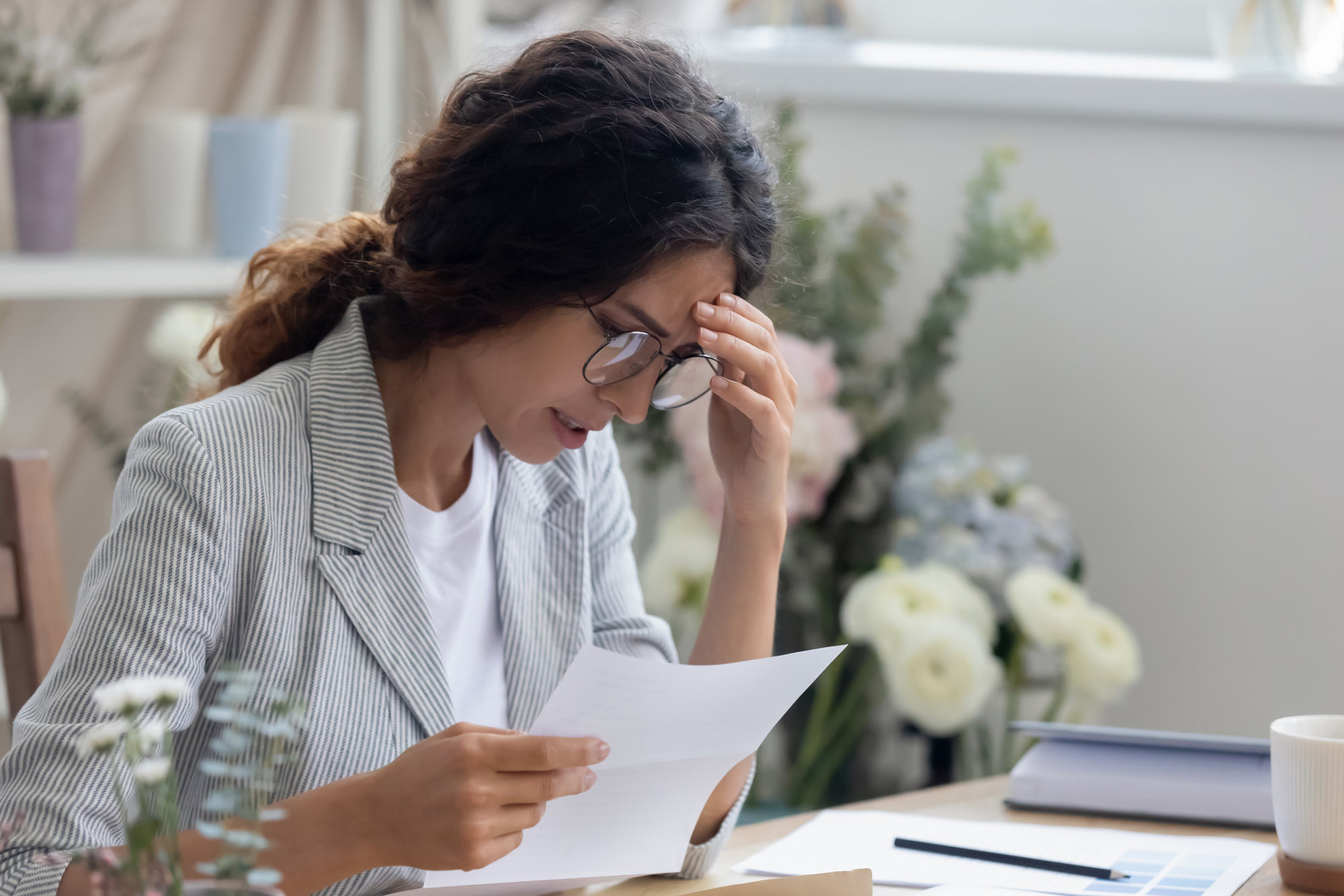woman looking at a document and holding her hand to her forehead in frustration