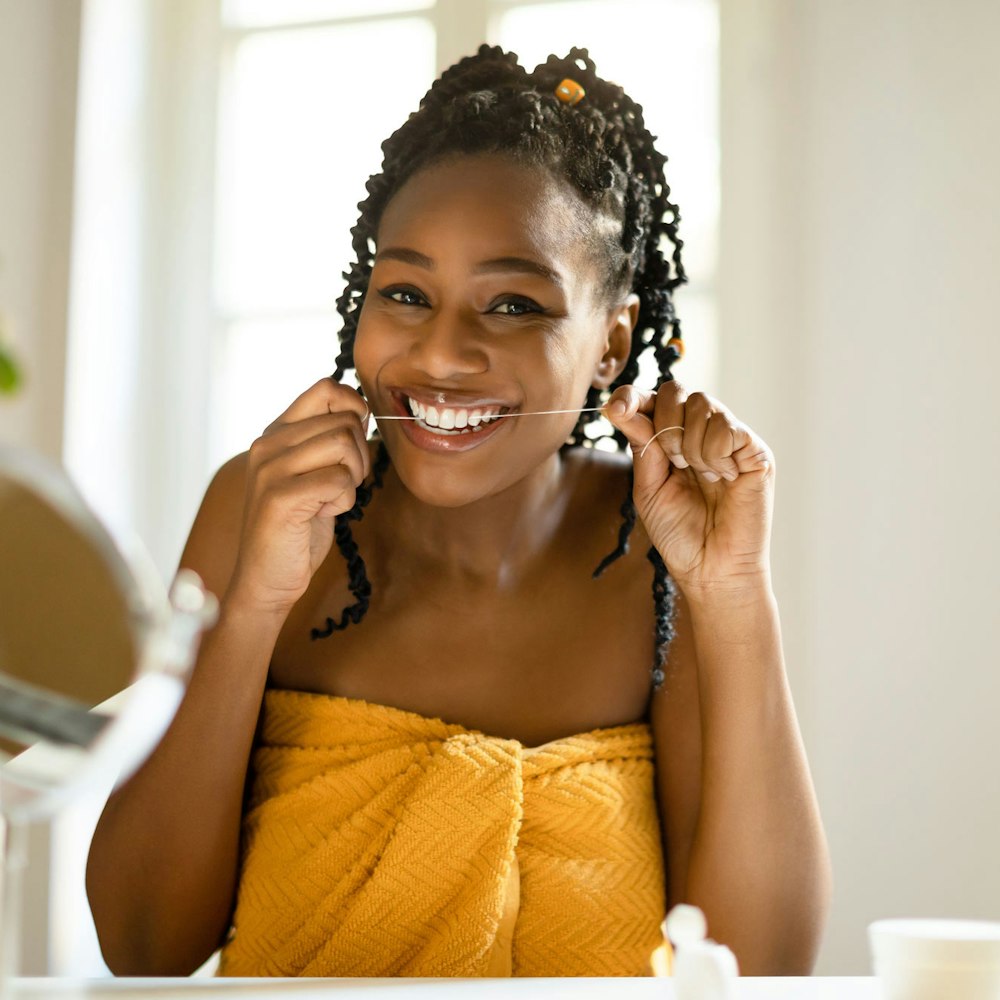 Smiling woman flossing her teeth with a yellow bathrobe