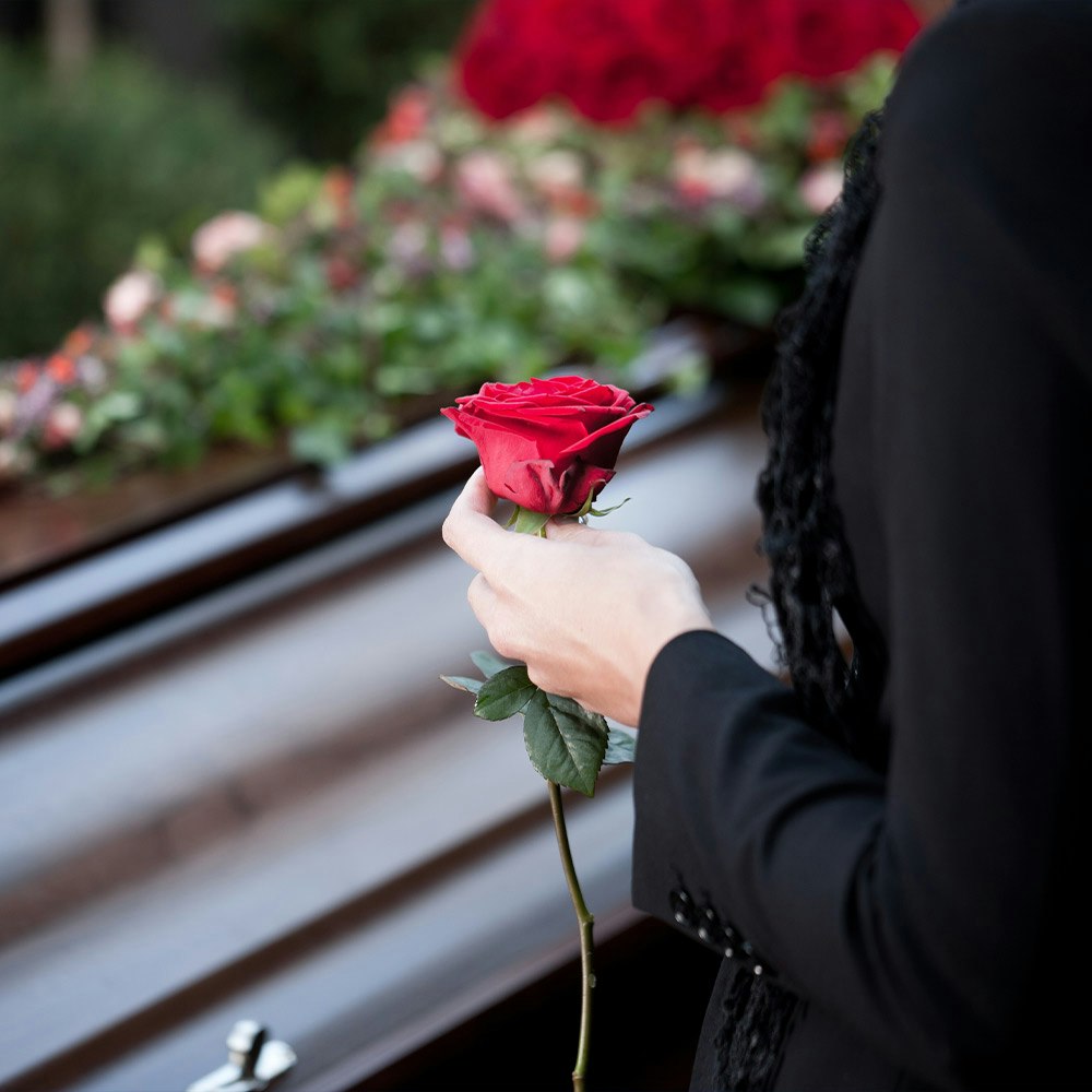 Loved one holding red rose in front of casket