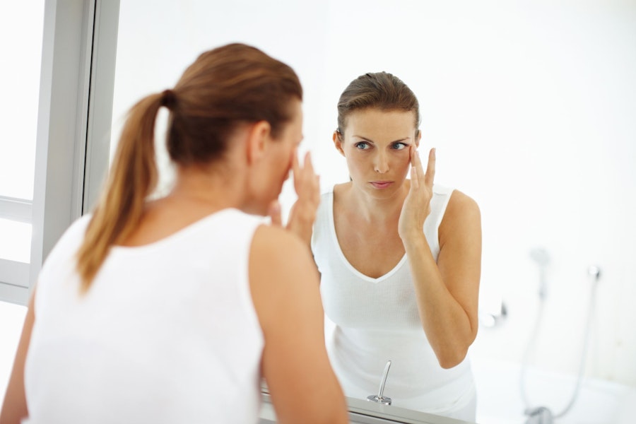 Woman looking in mirror and applying face cream