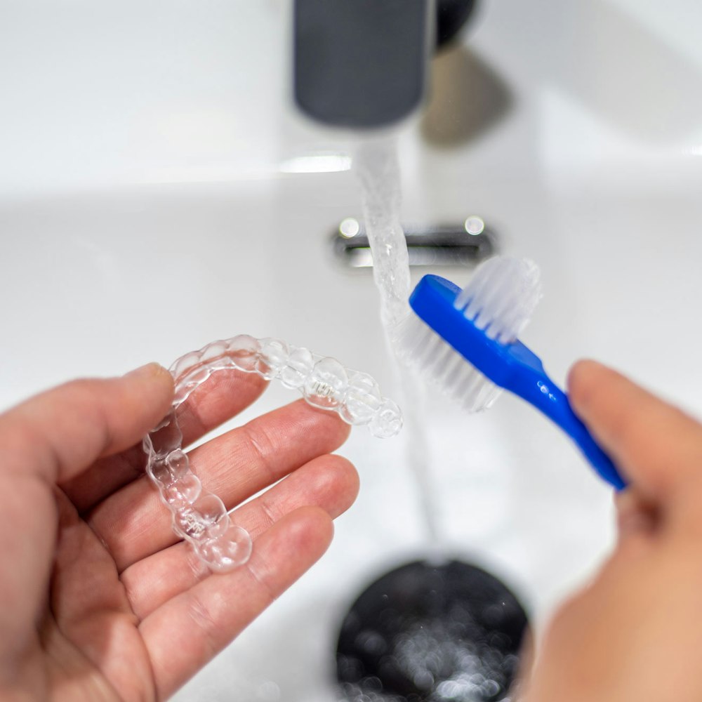 Person cleaning aligner with soft-bristle toothbrush