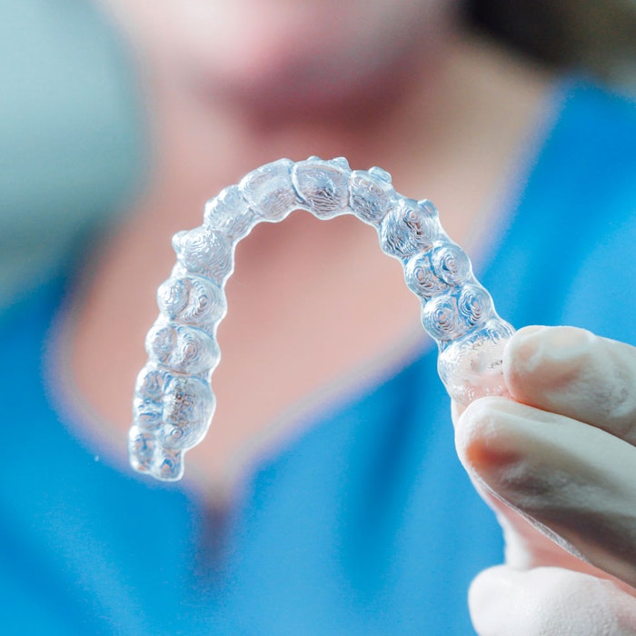 Hand holding a clear Invisalign aligner
