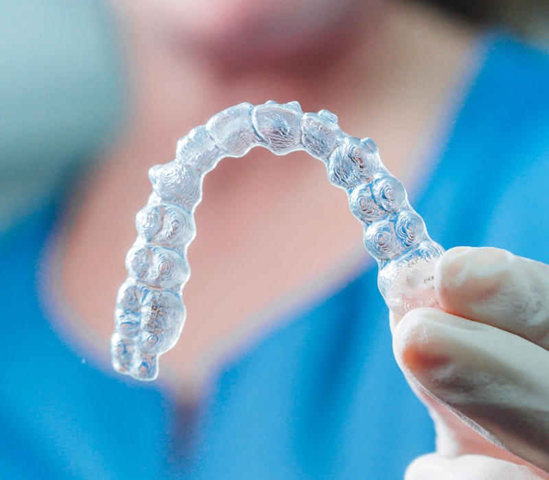 Hand holding a clear Invisalign aligner