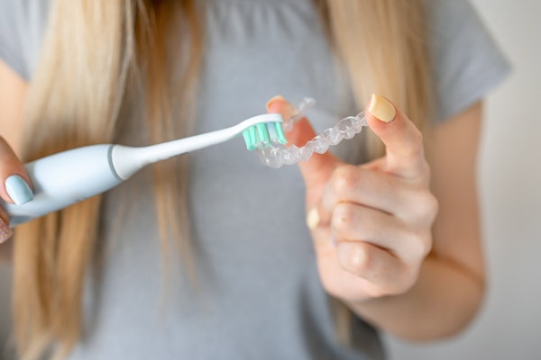Woman cleaning invisalign aligner with toothbrush