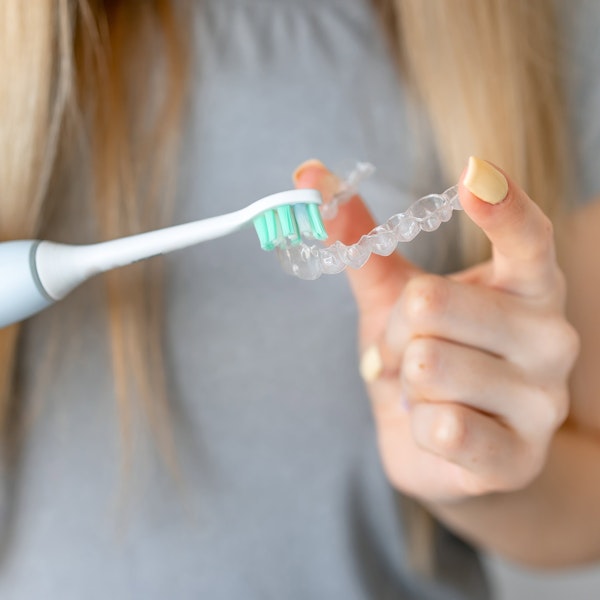Woman cleaning invisalign aligner with toothbrush