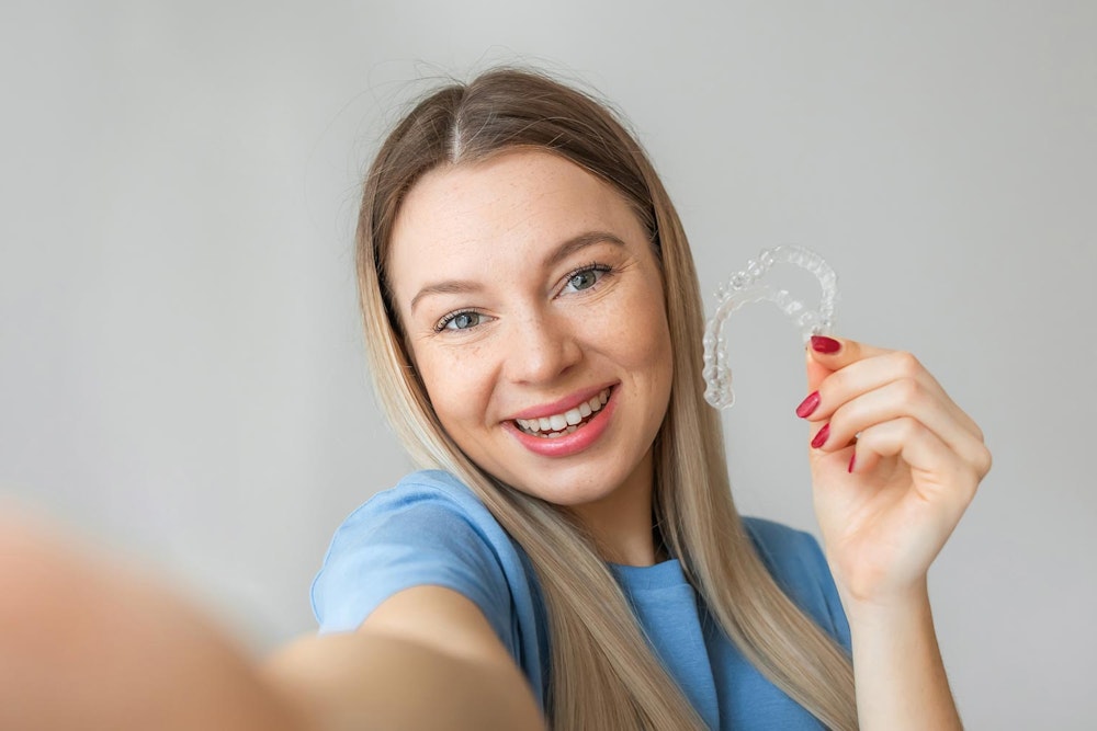 Smiling woman taking a selfie and holding her retainers