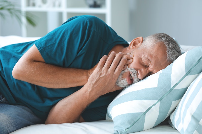 Guy holding jaw in pain in bed