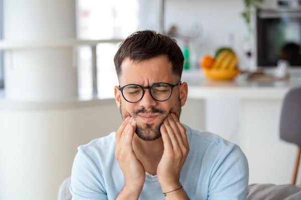 Man wearing glasses holding teeth in pain and in need of a root canal