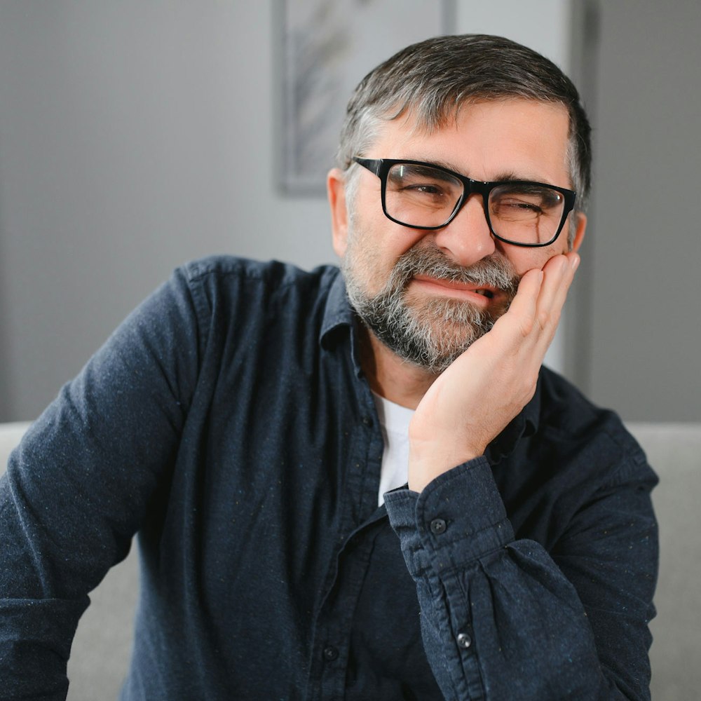 man with glasses holding jaw in pain