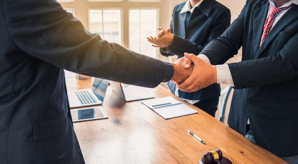 Mediator shaking hands with client while other party claps