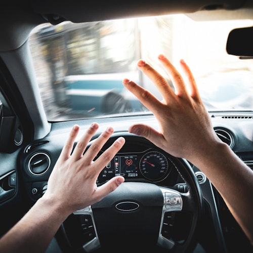 Driver holding up their hands protectively at the wheel