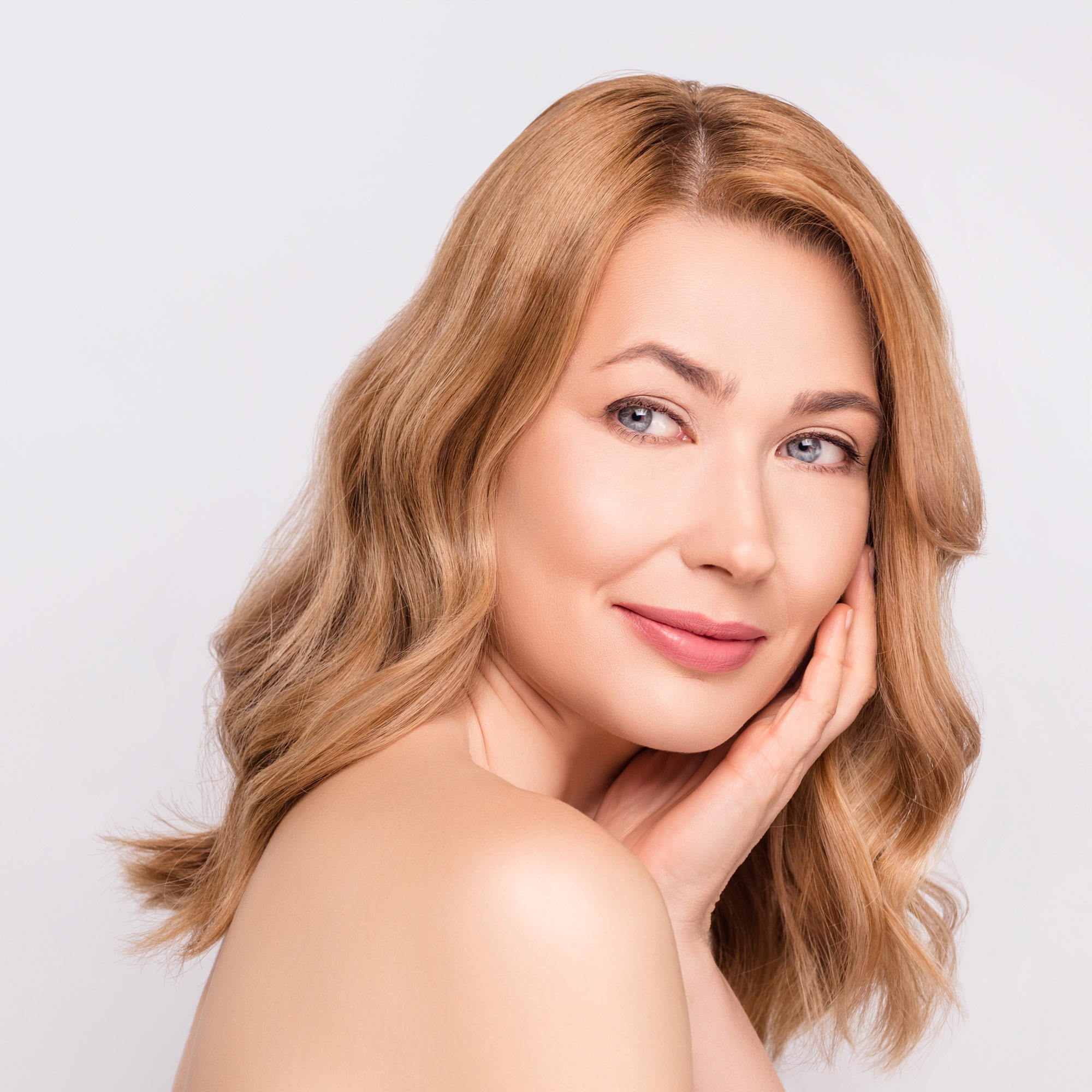 woman touching face and looking over her bare shoulder