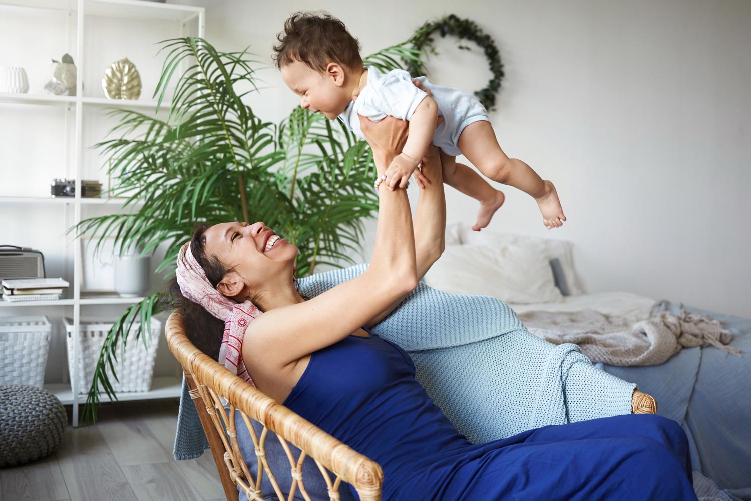 Mother lifting baby up in arms while sitting at home