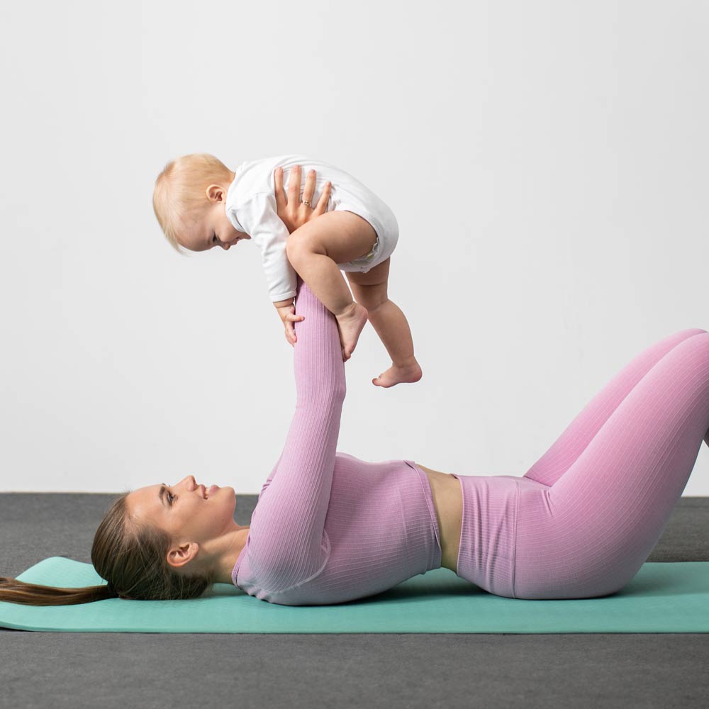 Woman lying down with liposuction holding up her baby